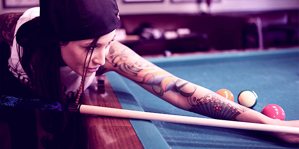 Women with tattooed arm sleeve playing pool with a pool cue that matches her look.