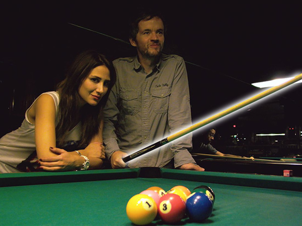 Guy with an attractive woman proudly shows off his pool cue at the pool hall.